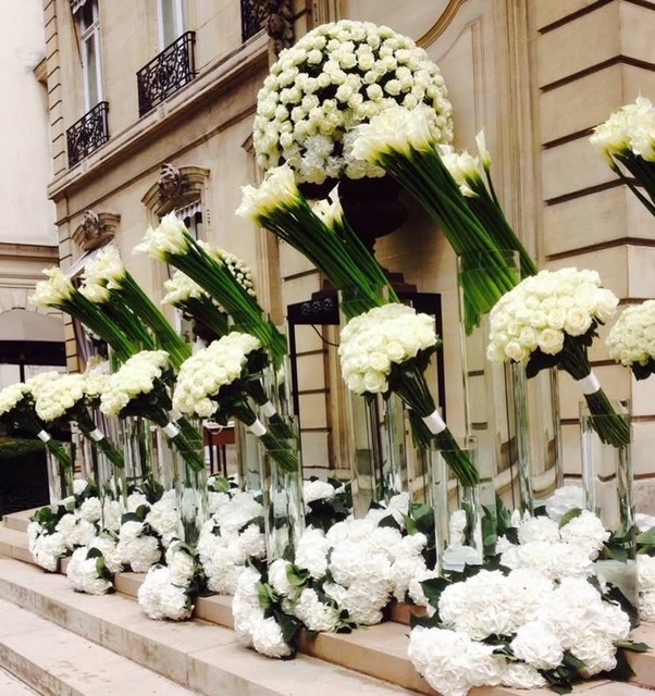 Bvlgari Paris Fashion Week entrance — towering white calla lily and rose floral sculptures lining the steps of a Parisian hôtel particulier