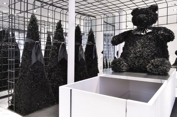 Alexander Wang flagship installation — black topiary cones with satin bows and a large black floral teddy bear sculpture on a white plinth